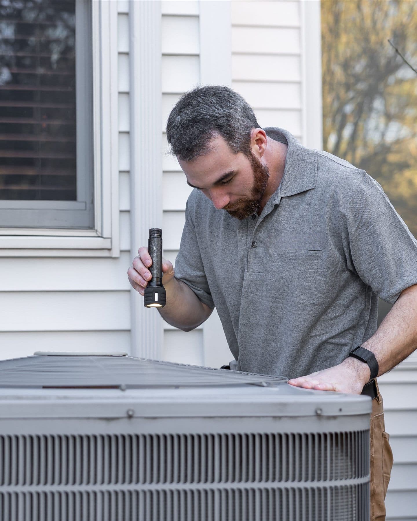 HVAC technician inspecting an outdoor AC unit at a home
