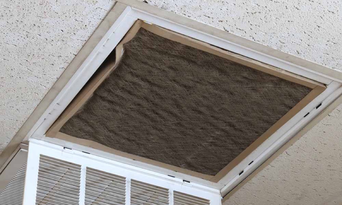 A pleated ceiling return-air filter loaded grey with dust, still installed in the return grille