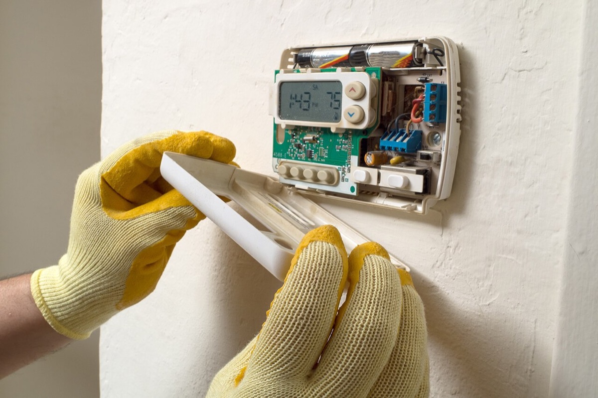 A thermostat with its cover removed during service, showing the wiring terminals and circuit board behind the display